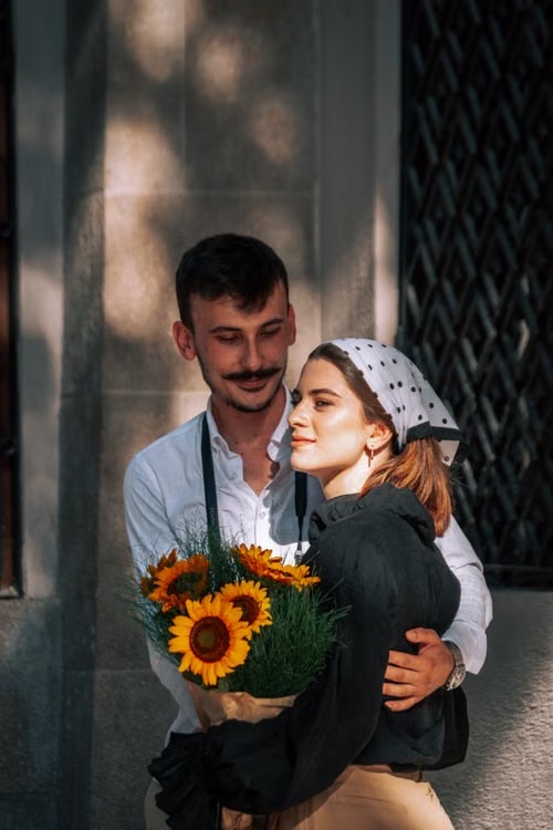 Claire and Adrien embracing with a bouquet of sunflowers